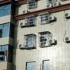 Exterior of a building with multiple air conditioners and window cages.